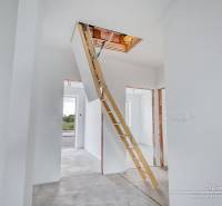 White interior of a family house with built-in attic stairs and gray flooring.