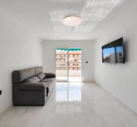 Living room of a three-room apartment with a gray sofa and a TV on the wall.