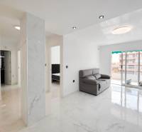 Living room in a three-room apartment with tiles and a couch, illuminated by large windows.