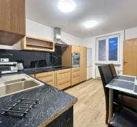A kitchen in a 2-room apartment with a wooden decor floor and black countertops.