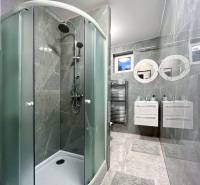 A bathroom in a 2-room apartment with ceramic tiles, a shower corner, and two sinks.