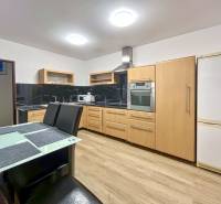 A kitchen with a wood-patterned floor in a 2-room apartment with appliances and a dining table.