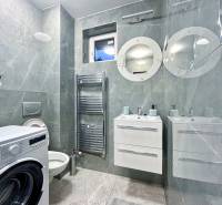 A bathroom with a washing machine and dark tiles in a 2-room apartment.