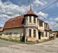 An older family house in Jasení, with a sloped metal roof on the corner of the street.