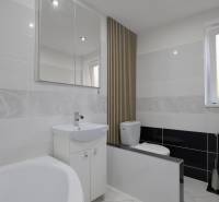 Bathroom in a 2-room apartment with light tiles, a bathtub, and a large mirror.
