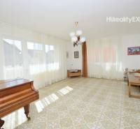 Living room in a family house with a piano, curtains, and a table on a tiled floor.