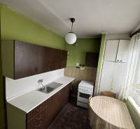 The kitchen of a two-room apartment with a wood-patterned floor, green walls, and a white stove.