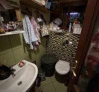 A small bathroom in a cottage with a sink, toilet, tiles, and a lot of toiletries.