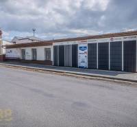 The building on Halatova Street in Poprad with a parking lot and trees in the background.