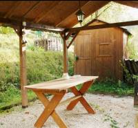Covered terrace with a table in the garden in Budatín, Žilina, next to a wooden cottage.