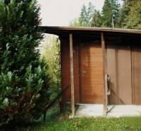 A wooden cottage in the gardens in Budatín, Žilina, with greenery in the background and trees.