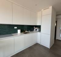 A kitchen in a villa with white cabinets, green tiles, and a view of the terrace.