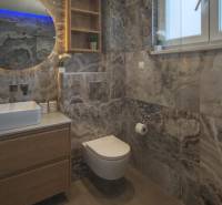 A bathroom in a villa with modern elements, marble tiles, a wall-hung toilet, and a sink.