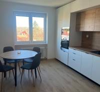 Dining nook with a round table and kitchen unit, floor with wooden decor.