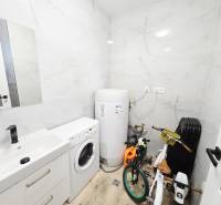 A bathroom with a sink, a washing machine, a boiler, and children's bicycles in a family house.