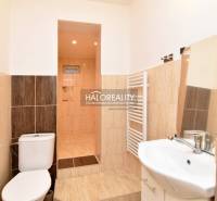 Bathroom in the Gardens with a toilet, shower, and sink, light tiles.