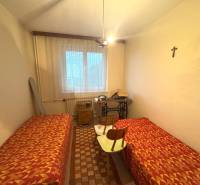 Izba v rodinnom dome s dvomi posteľami, šijacím strojom a krížom na stene.