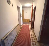 Chodba v rodinnom dome s kobercom a bielymi stenami, drevený nábytok vzadu.