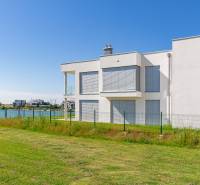 White object by the water, Kittsee, Am Seepark, with a grassy plot and a fence.