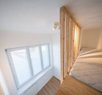 Loft bed in a 2-room apartment with a wooden-patterned floor and a large window.