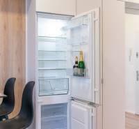 An open fridge with champagne next to a table and chairs in a 2-room apartment with wood-patterned flooring.