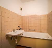 A bathroom in a 3-room apartment with a bathtub and a sink, tiled with beige tiles.