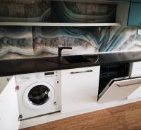 A kitchen with a dishwasher, washing machine, dark countertop, and wood-patterned flooring.