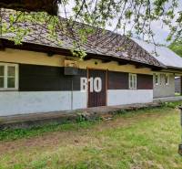 A wooden cottage in Necpaly with a traditional pump and an outdoor fireplace surrounded by greenery.