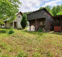 A cottage in Necpaly with a wooden shed surrounded by greenery and trees.