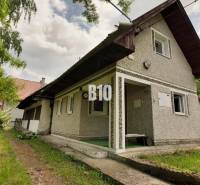 A cottage in Necpaly surrounded by greenery, with white plaster and a satellite dish.