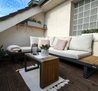 Outdoor terrace of a 3-room apartment with comfortable seating, plants, and flooring with a wooden decor.