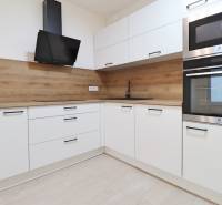 White kitchen with wood-patterned flooring and modern appliances in a 4-room apartment.