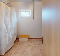 A wardrobe in a family house with clothes on hangers and a window at the top of the wall.