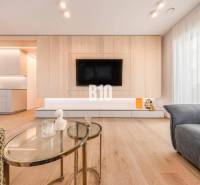 Living room in a three-room apartment with a wood-patterned floor and a TV on the wall.