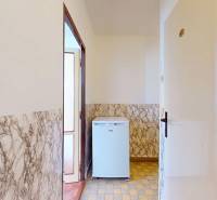 A hallway in a 3-room apartment with marble paneling and a small white refrigerator.