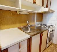 A kitchen in a 3-room apartment with a kitchen unit, stove, and sink, flooring with a wooden decor.