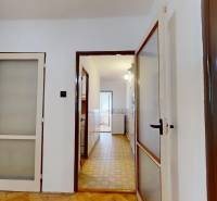 A hallway with entrances to rooms, a floor with a wooden decor, a visible kitchen in a 3-room apartment.