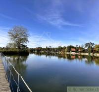 The lake near Malé Leváre with a wooden bridge and cottages in the background.