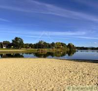 The beach by the cottage in Malé Leváre, surrounded by a lake and greenery on a sunny day.