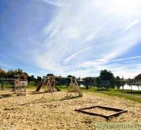 Playground by the lake in Malé Leváre with a blue sky and trees in the background.