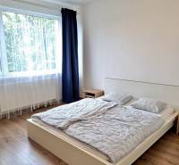 A bright bedroom with a large window, a bed, and a wooden decor floor in a 3-room apartment.