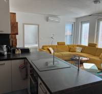 A bright living room of a three-room apartment with a yellow sofa and a kitchen island.