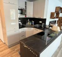 A kitchen in a two-room apartment with glossy cabinets and a floor with a wooden decor.