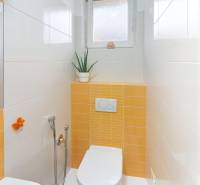 Bathroom in a family house with white and orange tiles, detailed toilet with decoration.