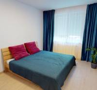 Bedroom in a family house with a bed, colorful pillows, and a floor with a wooden decor.
