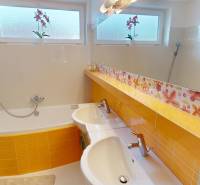 A bathroom in a family house with a bathtub, double sink, and decorative floral tiles.