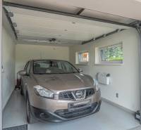 A car in the garage of a family house with white walls and two windows.