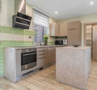 A kitchen in a family house with corners, cabinets, appliances, and green tiles.