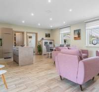 Open kitchen with living room in a family house. Light colors, pink armchairs, dining table.