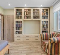 A library with books, a striped chair, and a bed in a family house.